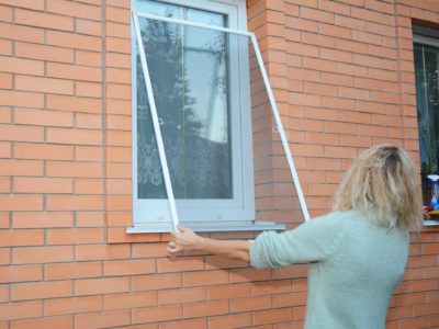 Woman removing window screen for cleaning wire screen on house window.