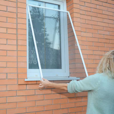 Woman removing window screen for cleaning wire screen on house window.