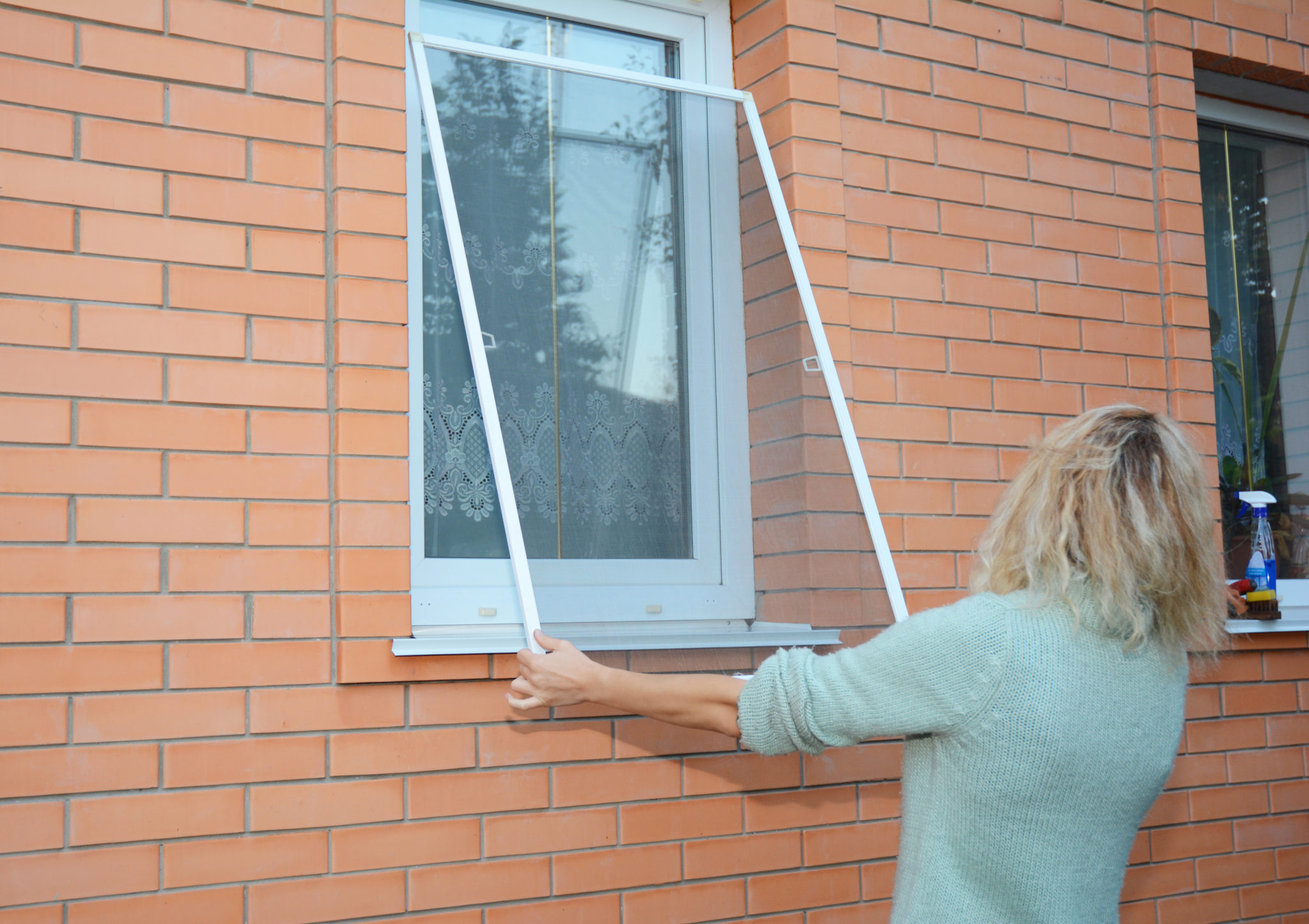 Woman removing window screen for cleaning wire screen on house window.