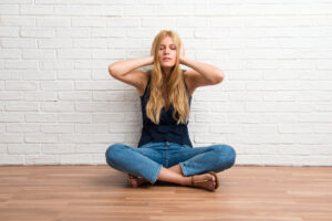 Woman sitting on a squeaking floor covering both ears with hands
