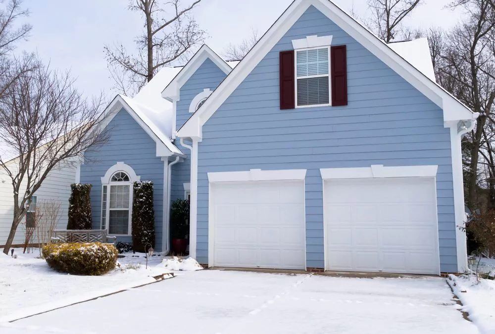 blue house with white garage doors in winter