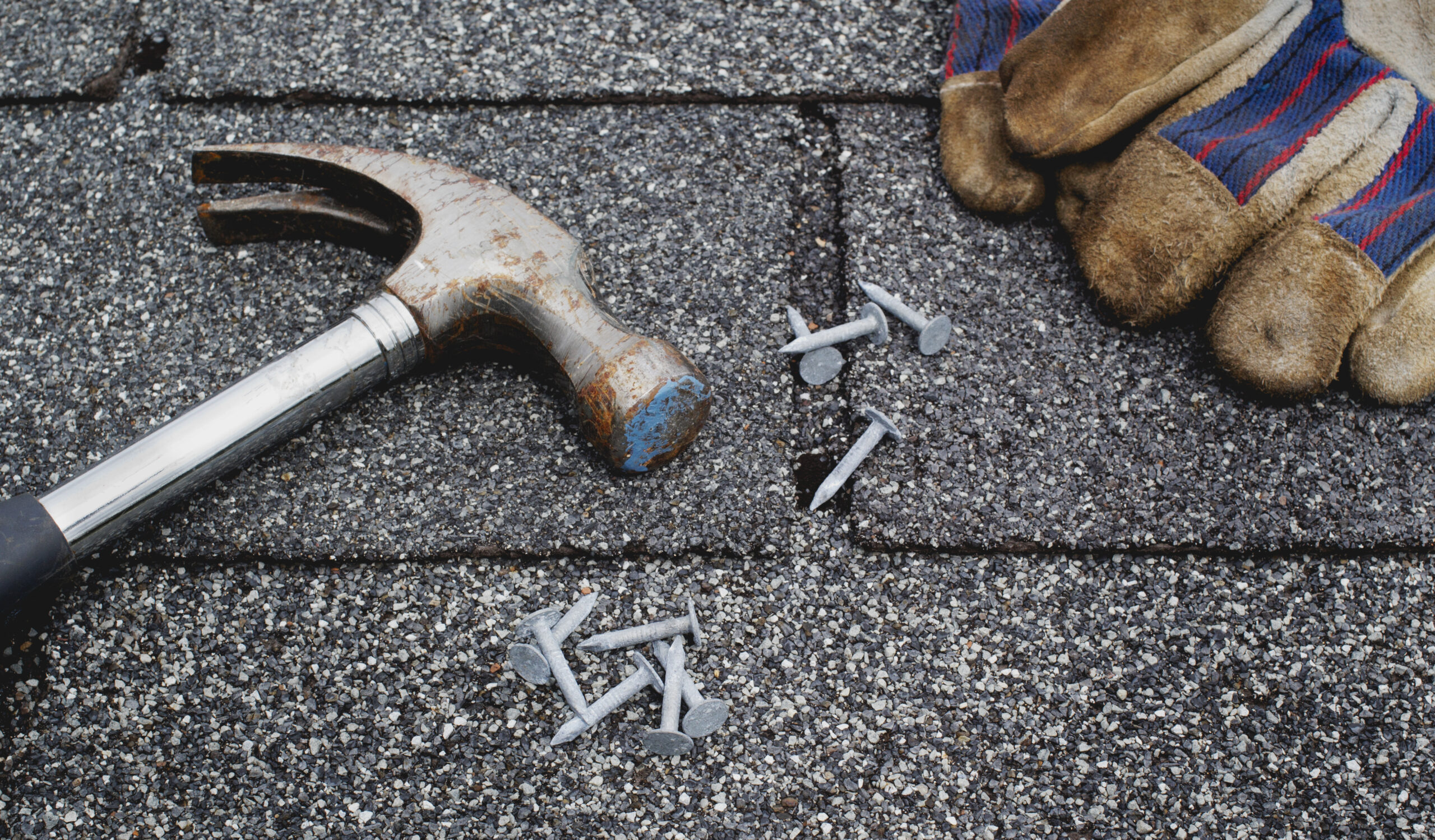 Hammer, roofing nails and work gloves on rooftop shingles