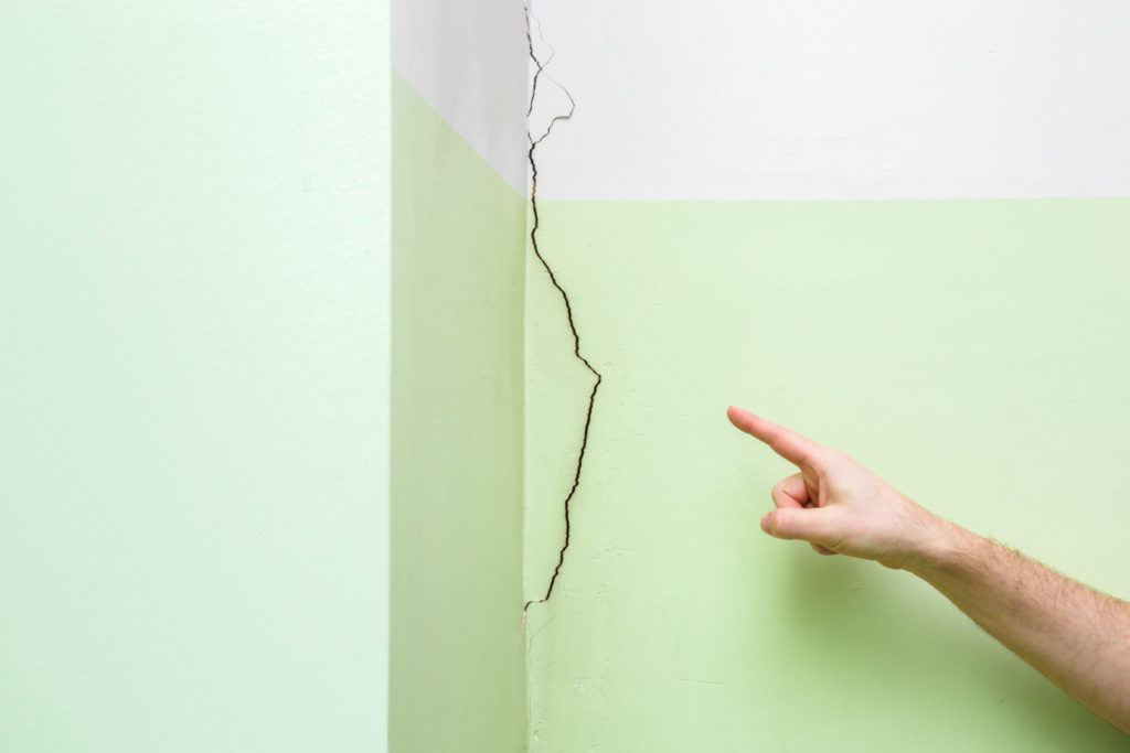 Man's hand finger pointing to cracked corner wall in house