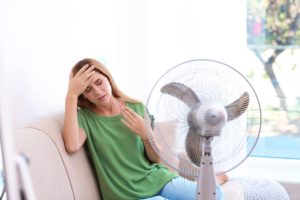 Woman suffering from heat in front of fan at home