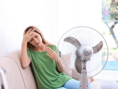 Woman suffering from heat in front of fan at home