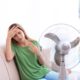 Woman suffering from heat in front of fan at home