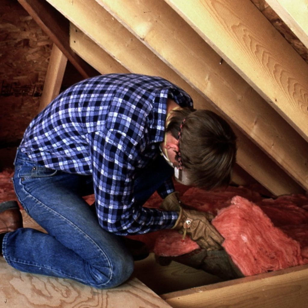 Man installing fiberglass insulation in attic.