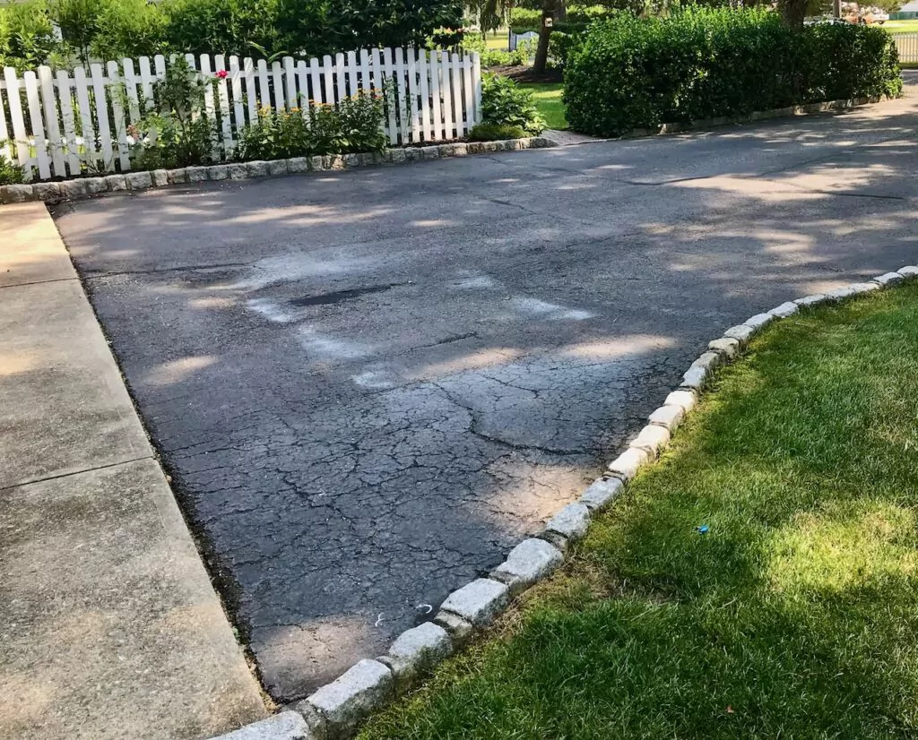 Asphalt driveway with gap between driveway and concrete garage apron.