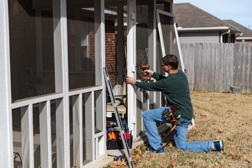 Man repairing a screened in back porch, patio, door.