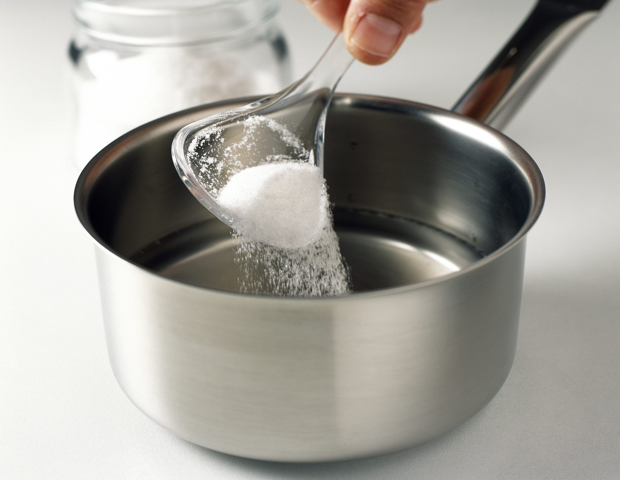 Sugar being poured into pot on stove