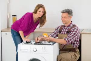 Woman Looking At Male Technician Checking Washing Machine In Kitchen