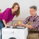 Woman Looking At Male Technician Checking Washing Machine In Kitchen