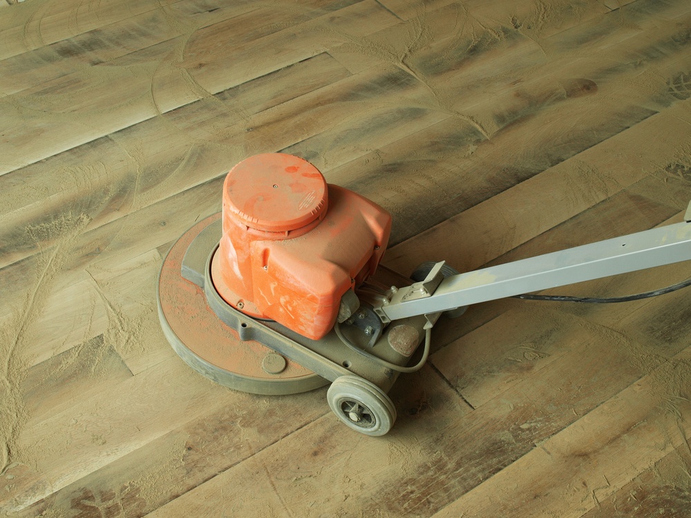 Using a floor buffer to sand and refinish a hardwood floor.