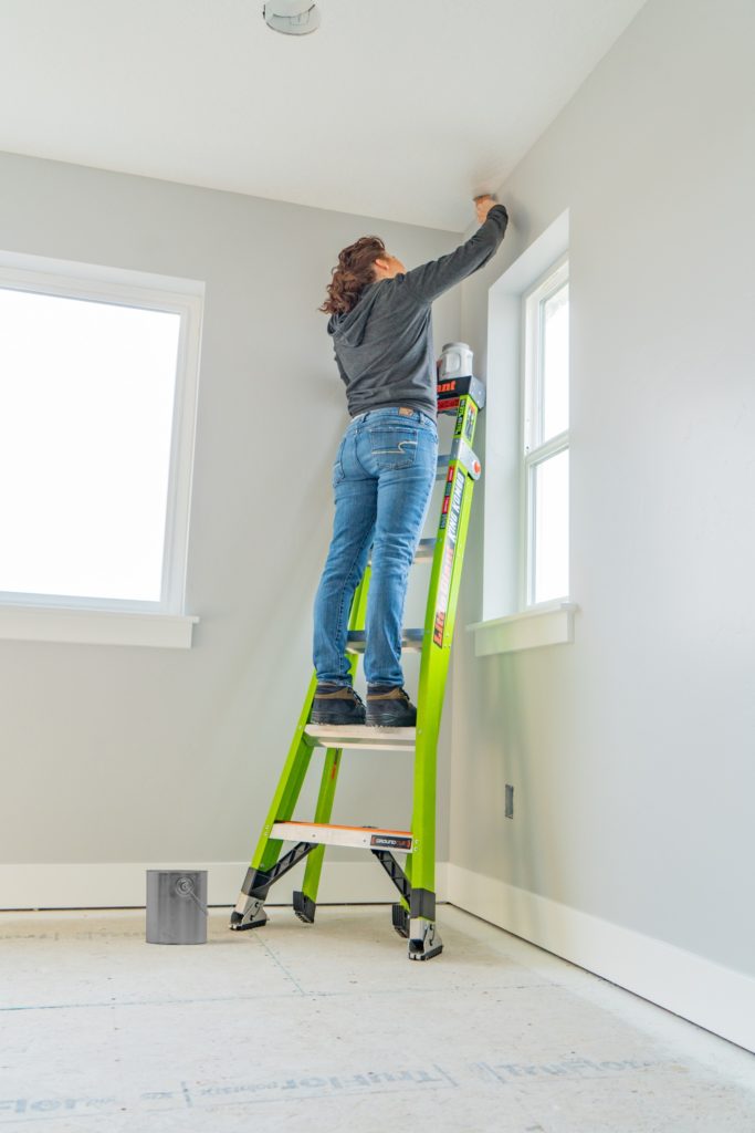 Woman standing on Little Giant King Kombo ladder painting an inside wall corner.