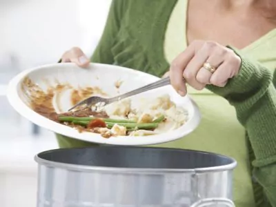 Woman Scraping Food Leftovers Into Garbage Bin