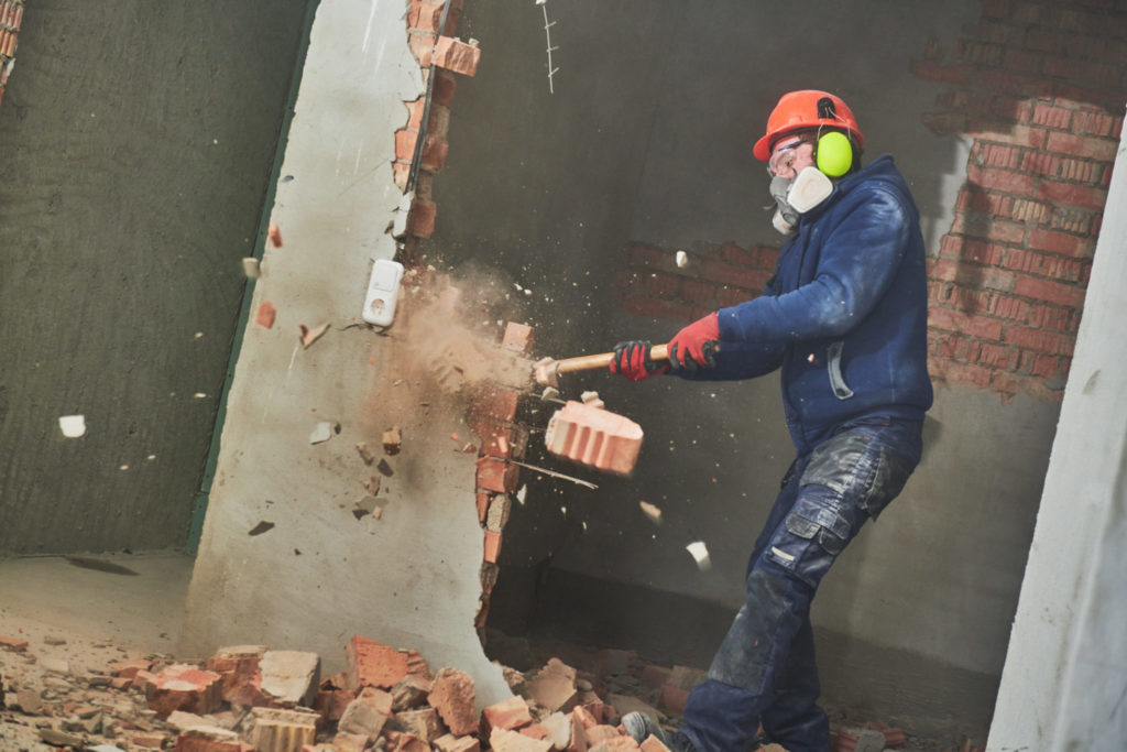 Man destroying wall with sledgehammer releasing toxic dust