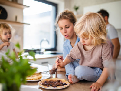 Young family with two small children indoors in kitchen, eating pancakes.