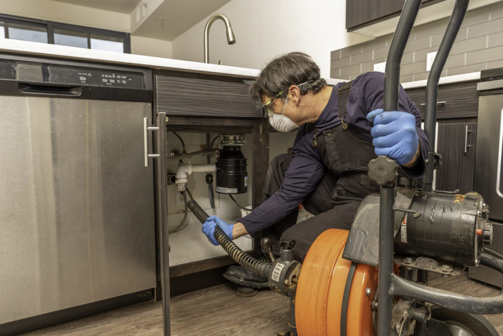 Plumber with Facemask Cleaning Drain