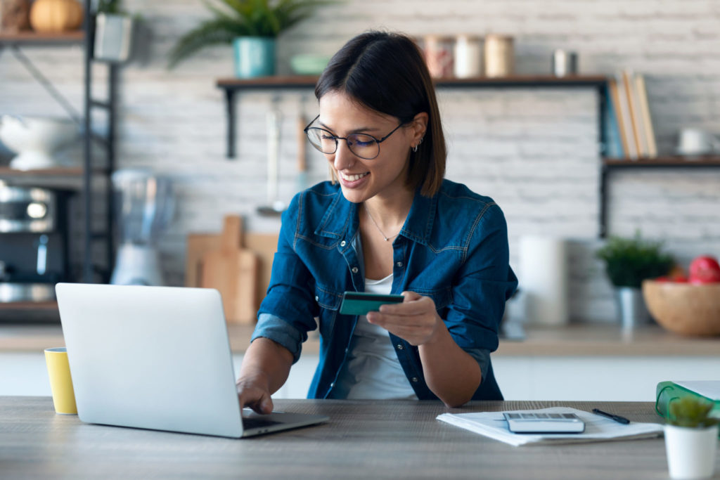 Woman holding white credit card for shopping in the kitchen at home.