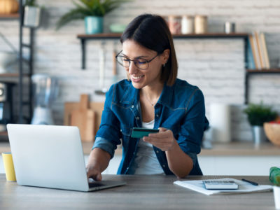 Woman holding white credit card for shopping in the kitchen at home.