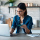 Woman holding white credit card for shopping in the kitchen at home.