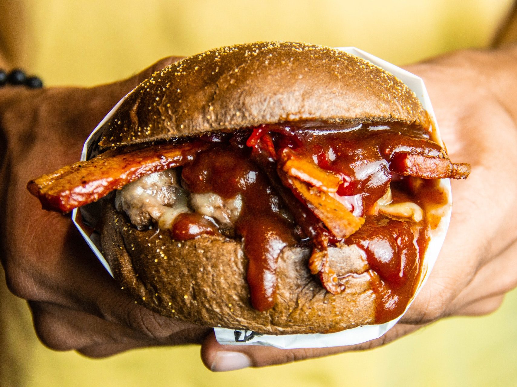 Person holding a juicy BBQ sandwich covered with barbeque sauce