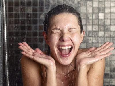 Young woman reacting in shock to hot or cold shower water