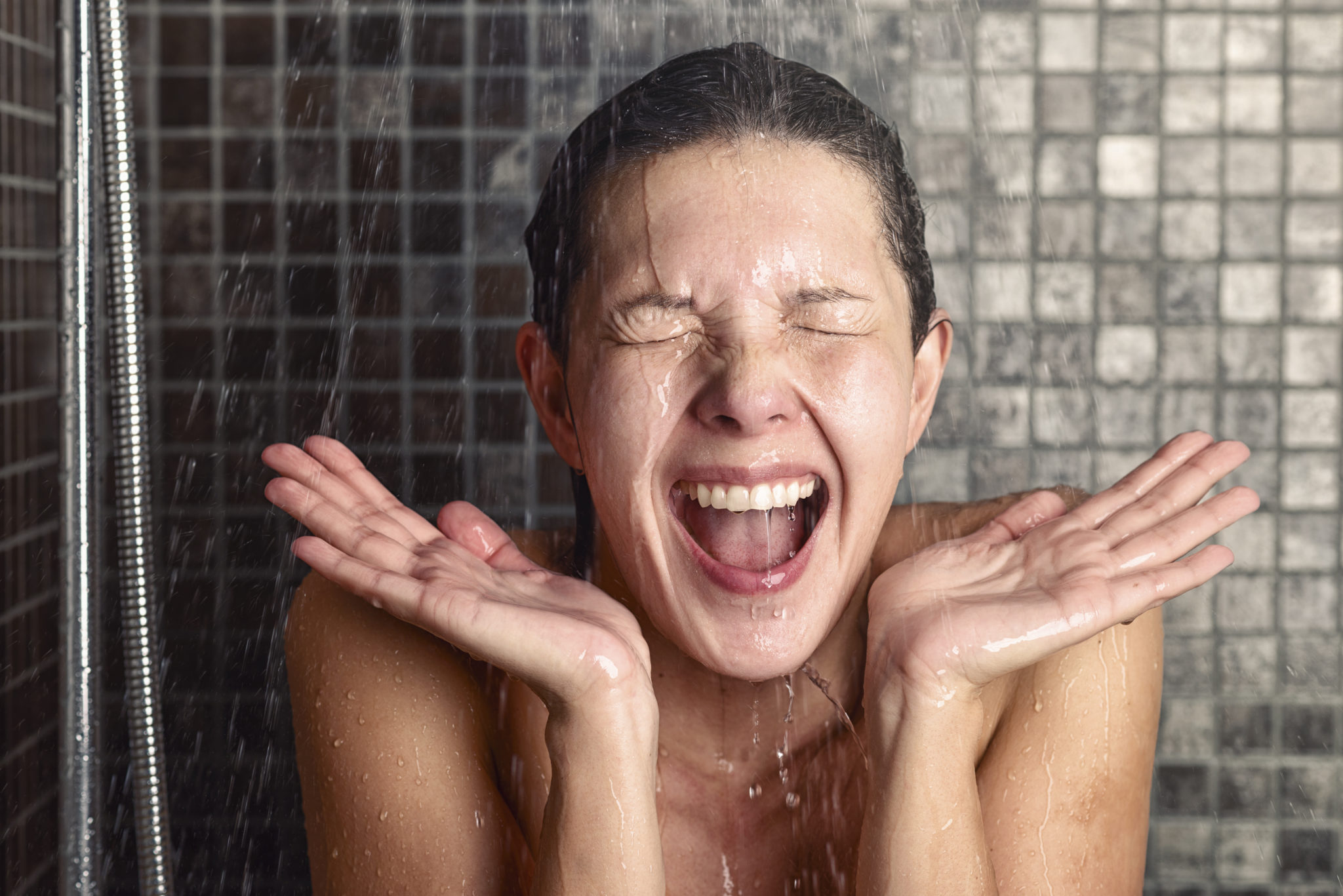 Young woman reacting in shock to hot or cold shower water