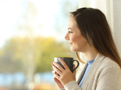 Woman holding coffee cup looks out through window on a cold day.