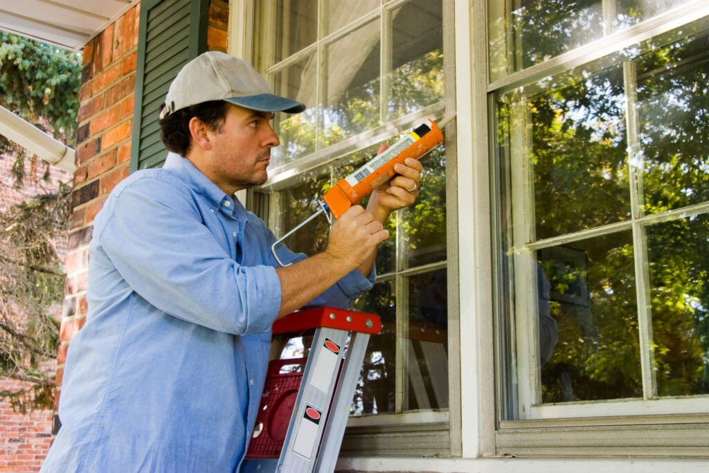 Man on ladder caulking outside window