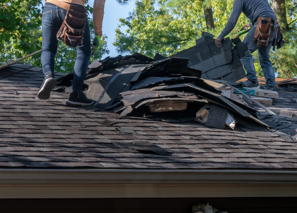 Workers removing old roof shingles on a house.