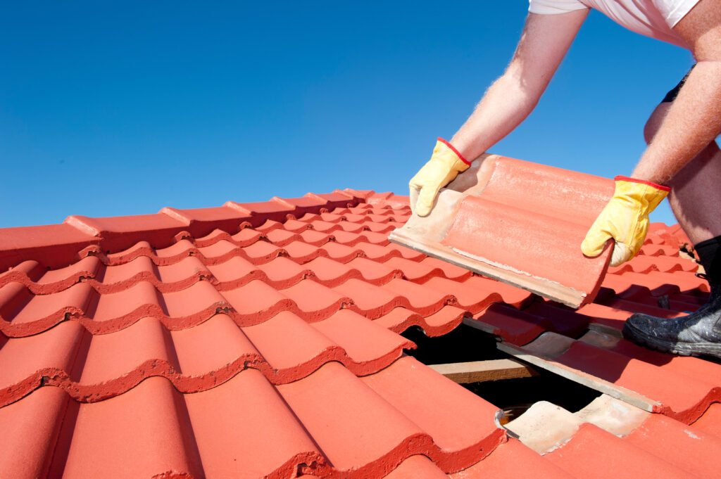 Roof repair, worker replacing red clay tile roof shingles.